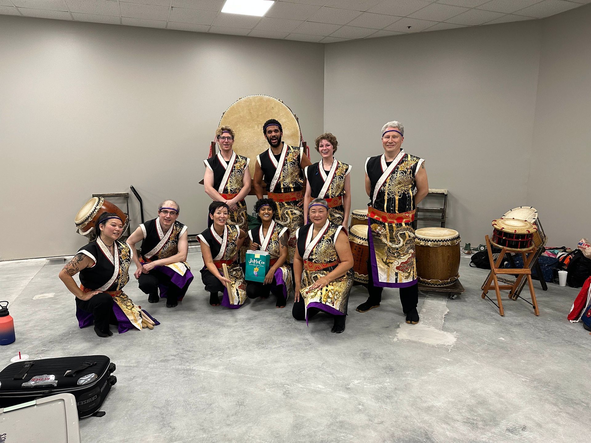 Group of people in traditional Japanese attire posing with taiko drums in a gray room.