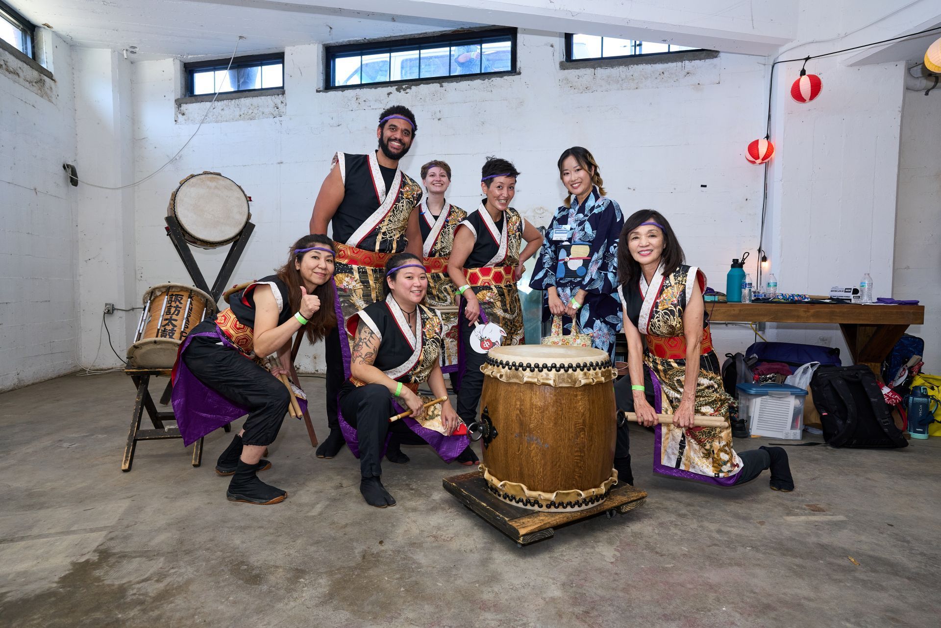 Group of people in traditional Japanese attire posing with taiko drums in an industrial setting.