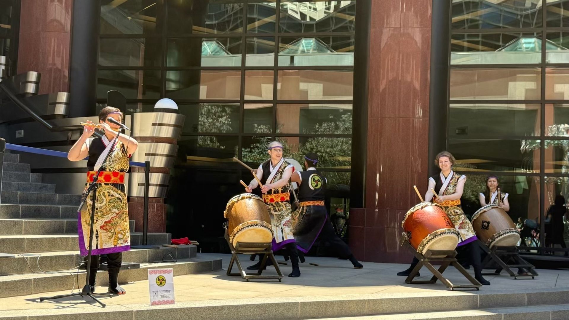 Japanese musicians performing on drums and flute outside a building.