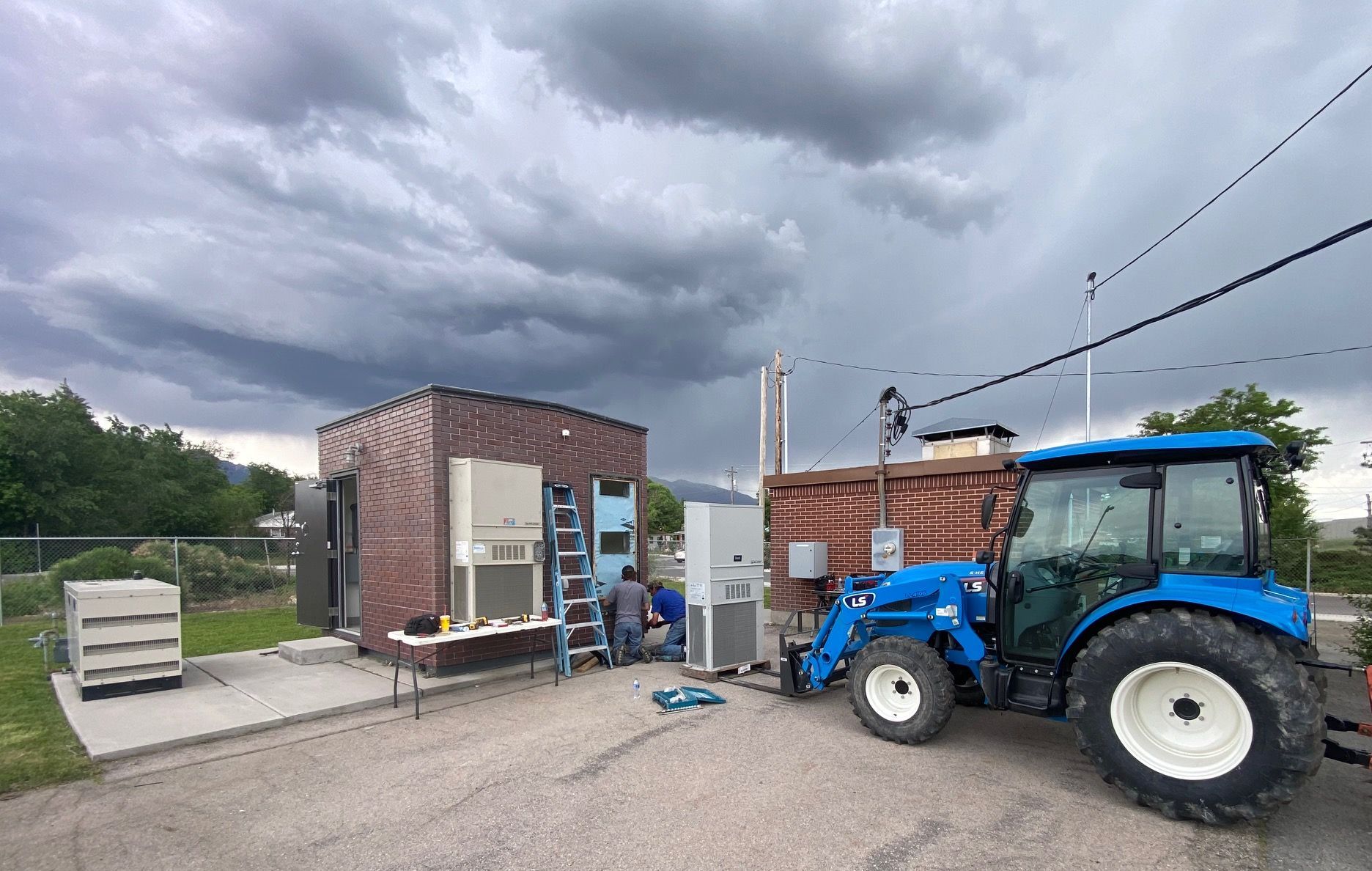 A blue tractor is parked in front of a brick building.