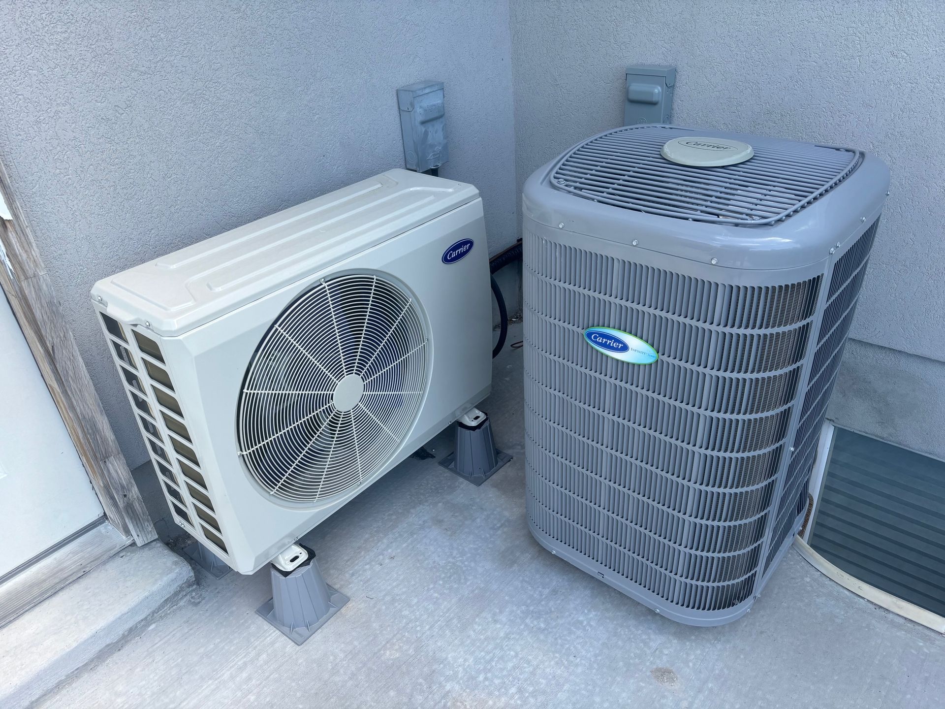 Two air conditioners are sitting next to each other on the side of a building.