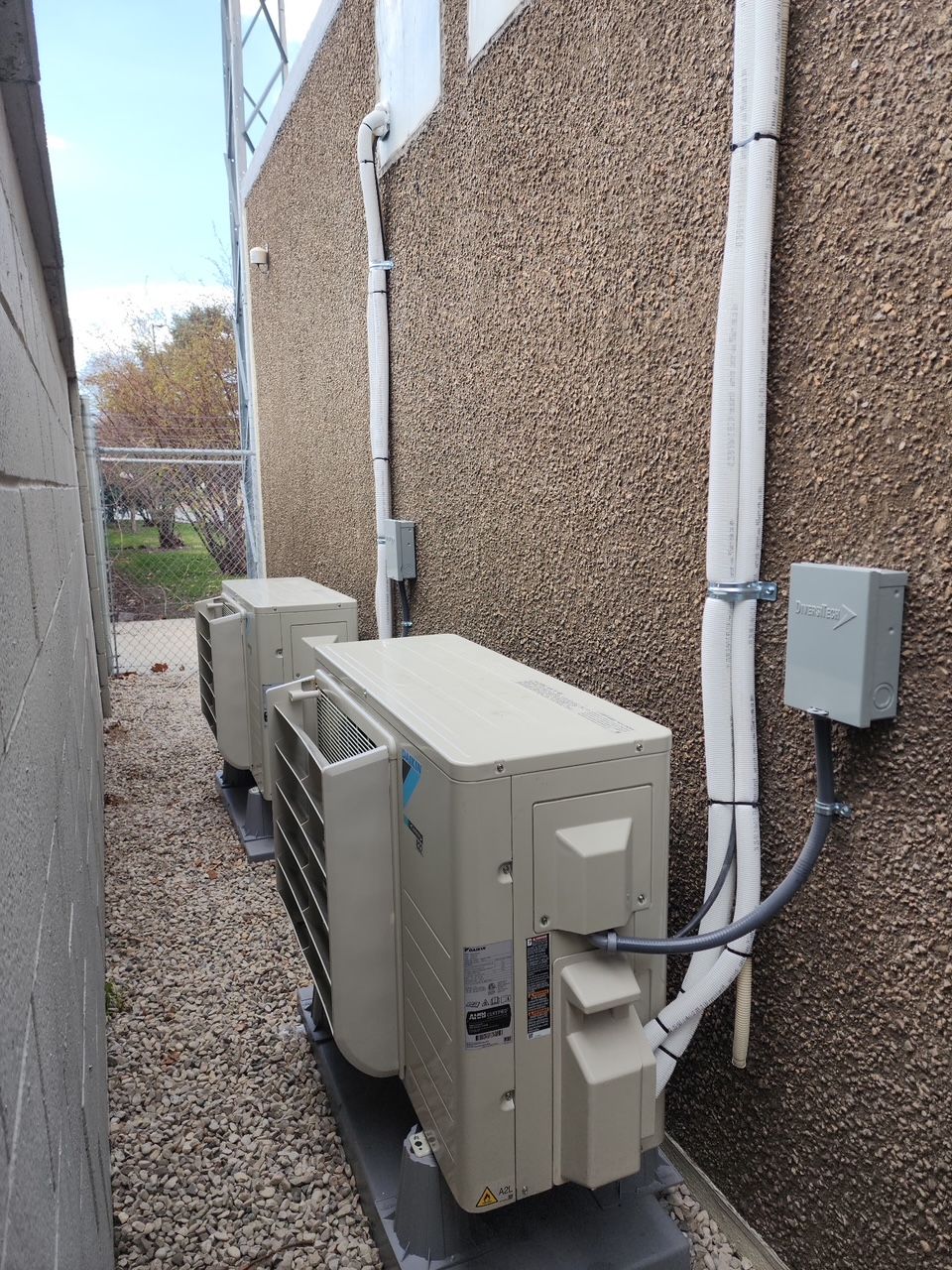 Two air conditioners are sitting next to each other on the side of a building.
