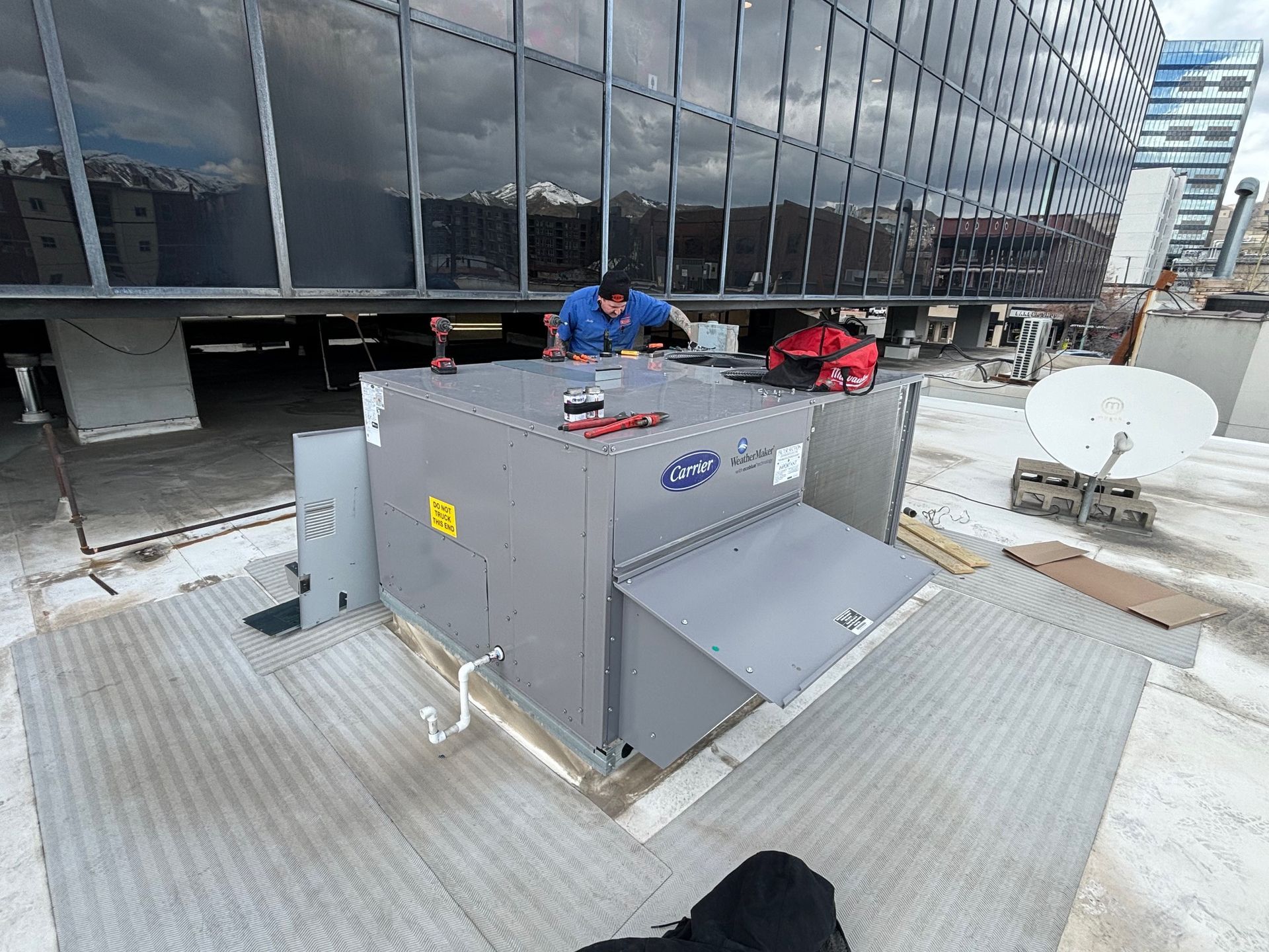 A man is working on an air conditioner on the roof of a building.