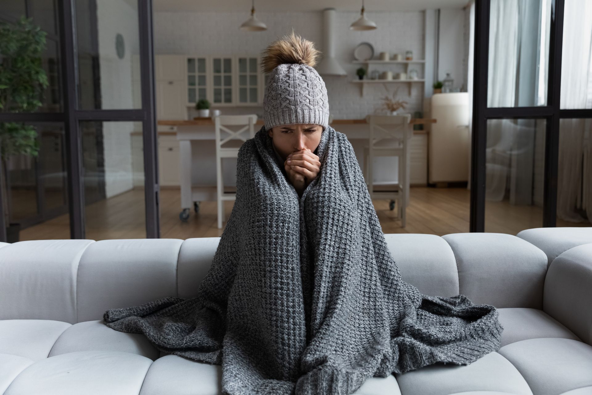 A woman is sitting on a couch wrapped in a blanket.
