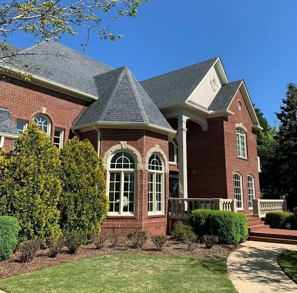 Red brick house with dark gray roof, arched windows, and manicured lawn under a blue sky.