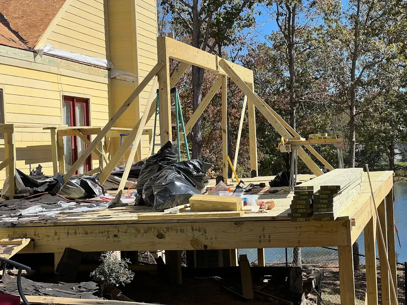 Deck under construction with wooden frame, overlooking a body of water, sunny day.
