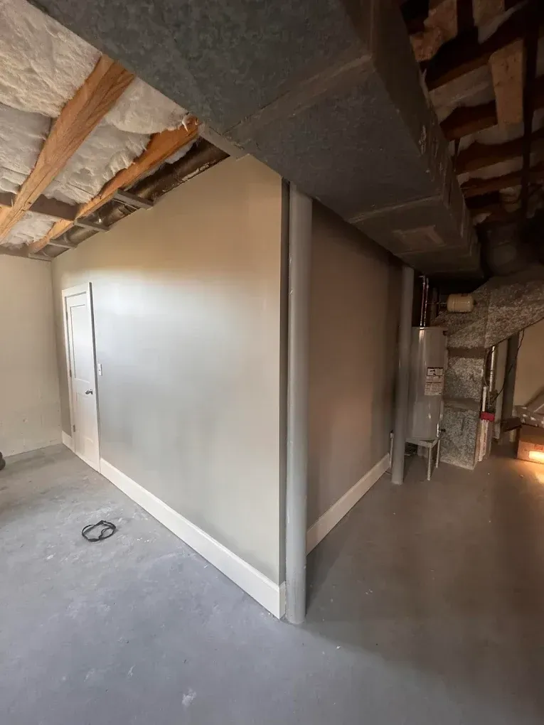 A newly painted room in a basement with concrete floors, white trim, and exposed ductwork.
