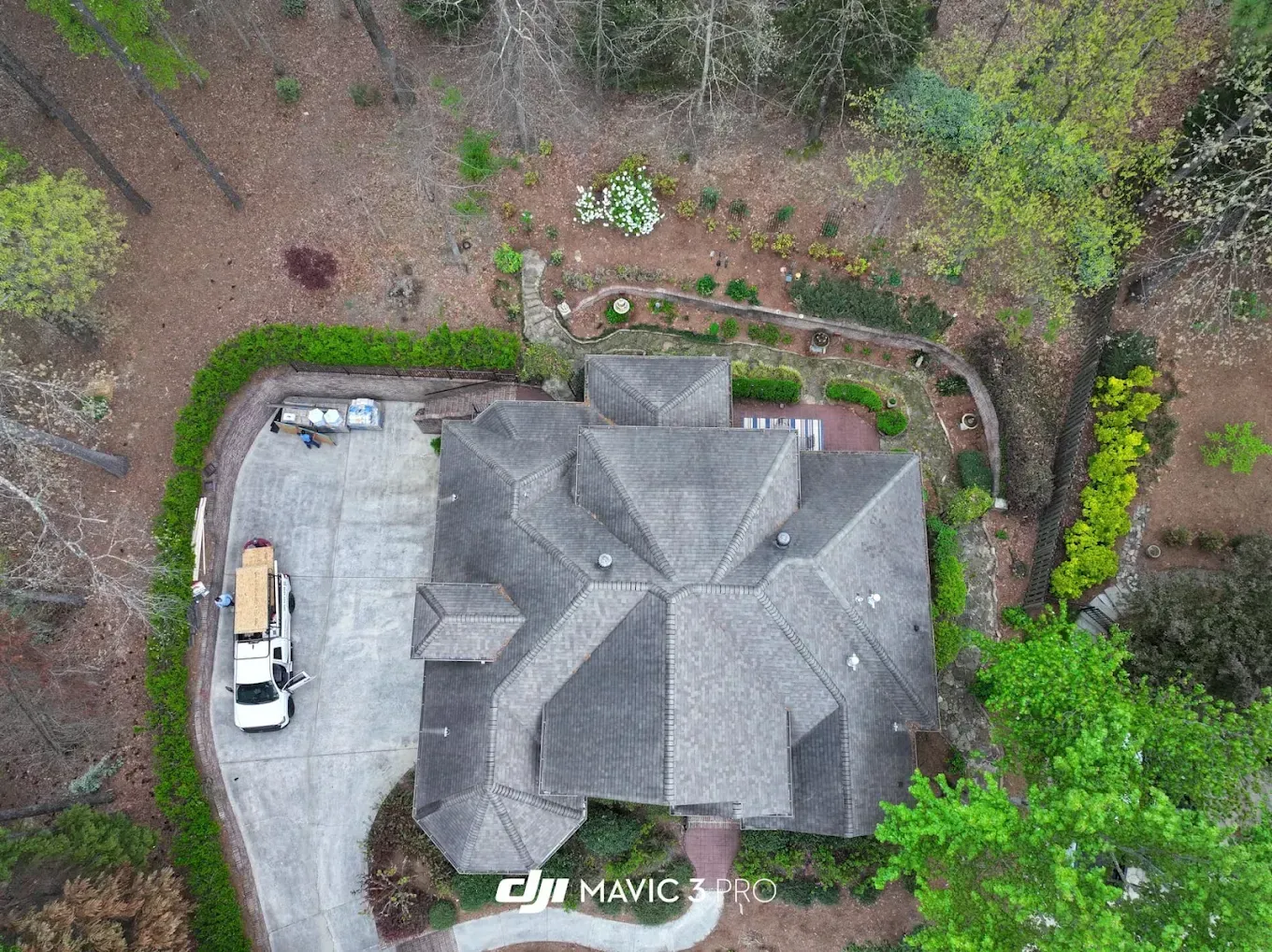 Overhead view of a house with a gray roof, surrounded by trees and a driveway with a truck.