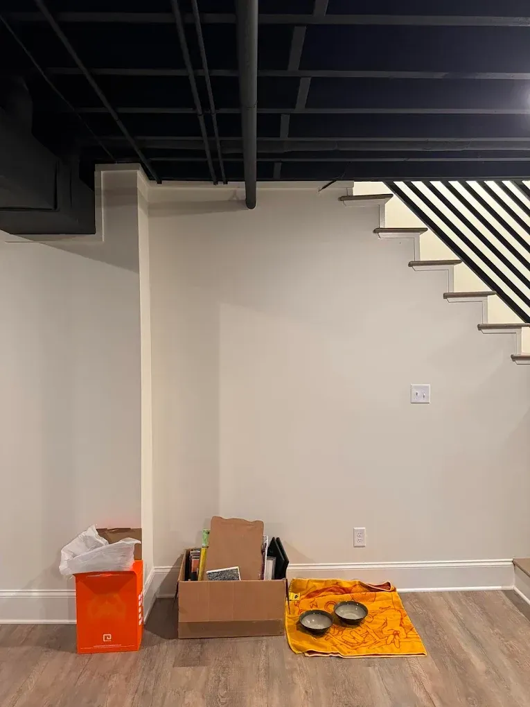 Empty basement corner with unfinished ceiling, stairs, and boxes.
