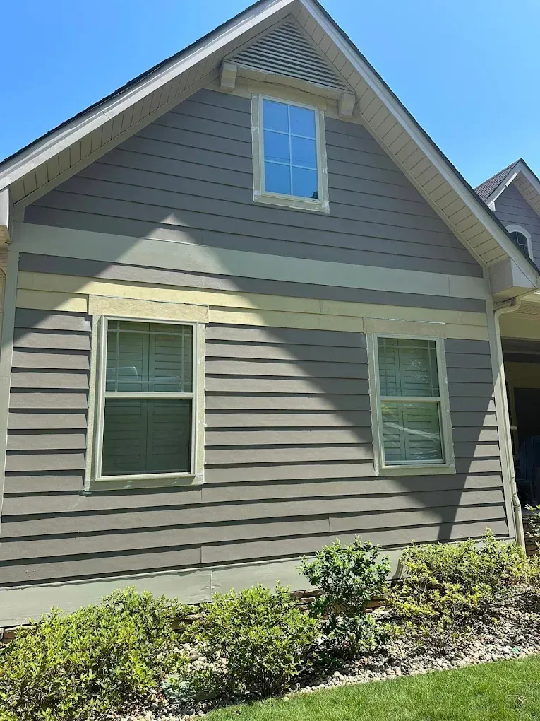 Gray house with two windows and a small upper window, bordered with light green trim and tan accent band.