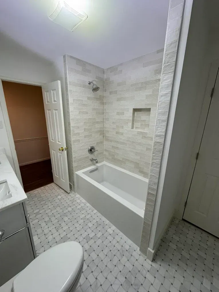 Bathroom with white tub, tiled shower, mosaic floor, and open door to a room.