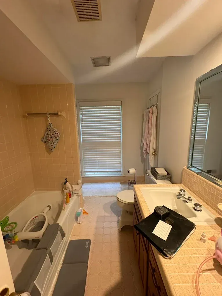 Bathroom with a bathtub, toilet, sink, and window with blinds.