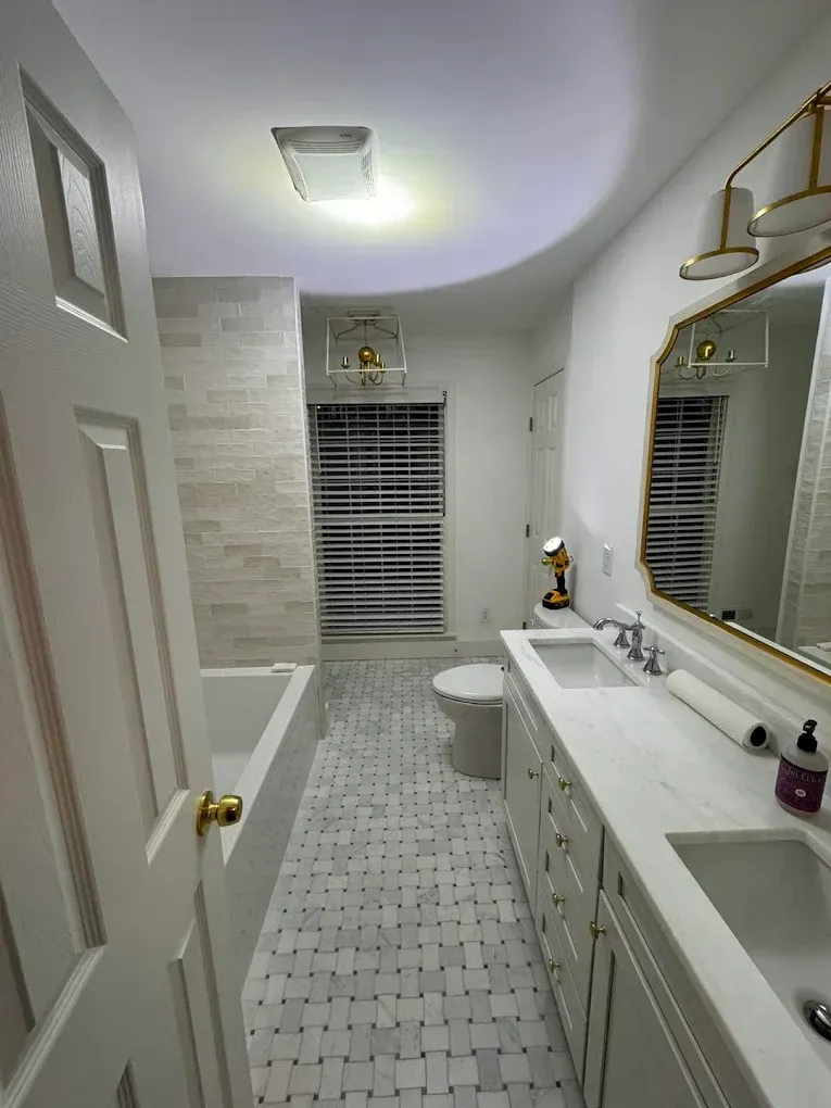 Bathroom with white cabinets, marble countertop, mosaic floor, gold mirror frame, and light fixtures.