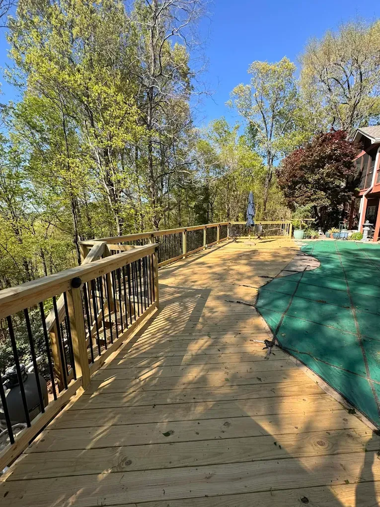 Wooden deck with black railings and light wood planks, overlooking trees and a blue sky.