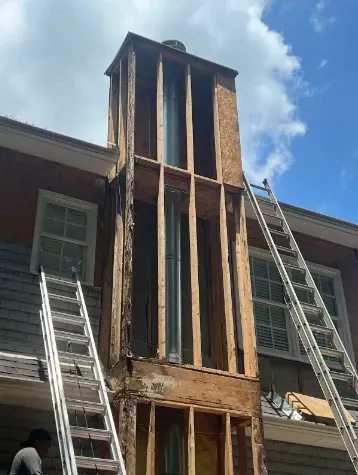 Chimney under construction on a house, with exposed wooden frame. Ladders are present.