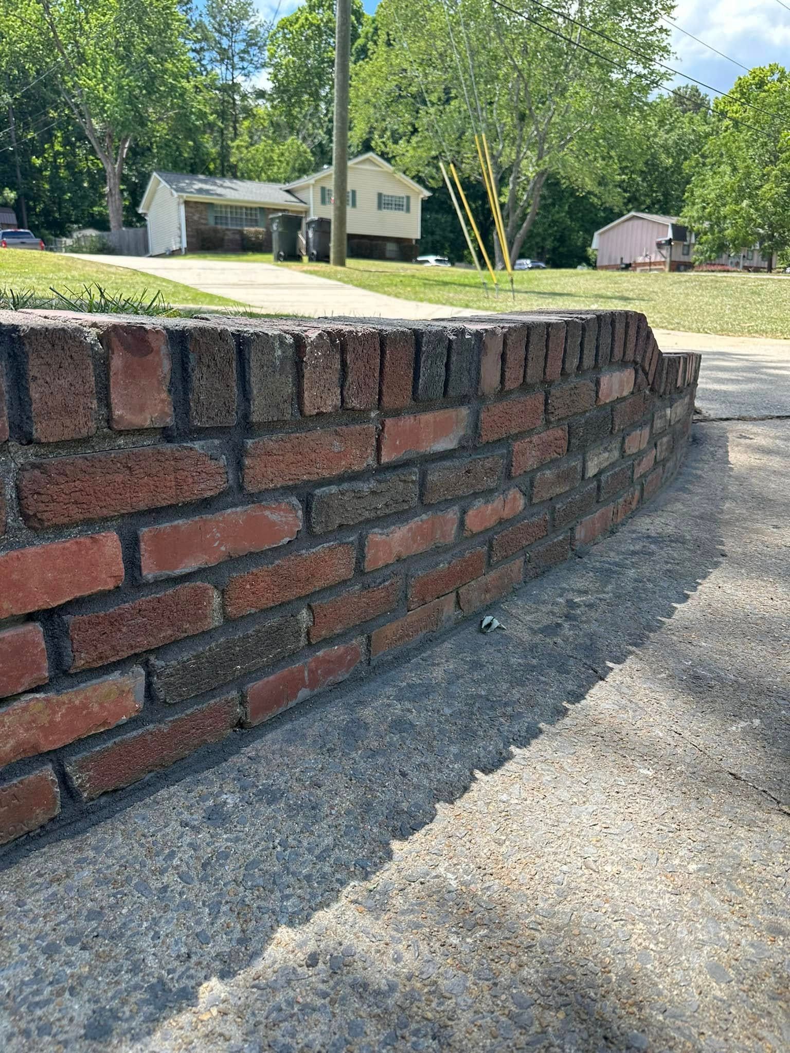 Low brick wall along a sidewalk, with houses and trees in the background on a sunny day.