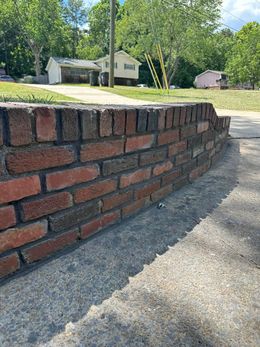 Low brick wall along a sidewalk, with houses and trees in the background on a sunny day.