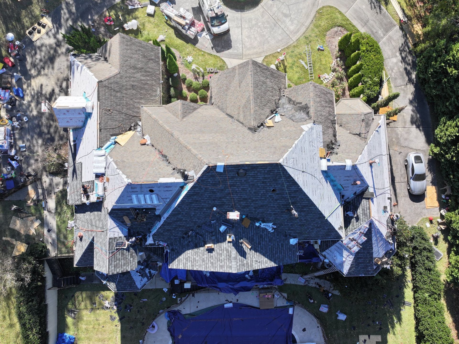 Overhead view of a house with a complex roof, tarp covers, debris, and a pool.