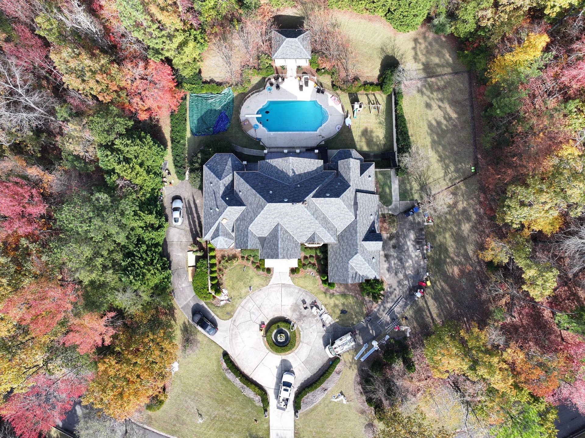 Aerial view of a large house with a pool surrounded by colorful autumn trees.