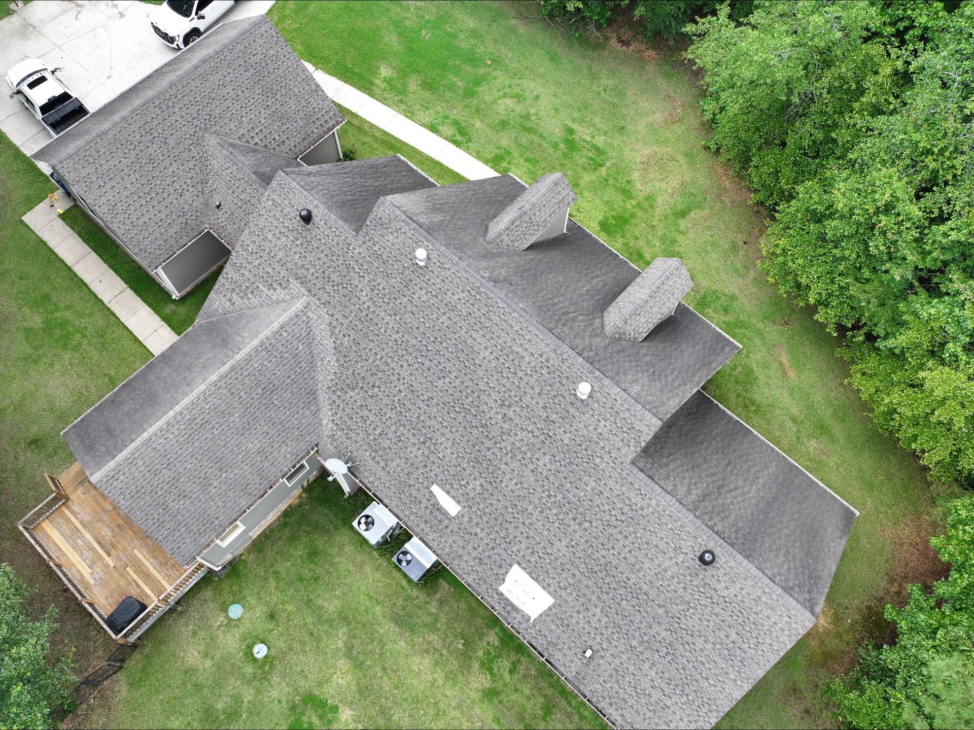 Overhead view of a house with a gray shingle roof, surrounded by green grass and trees.
