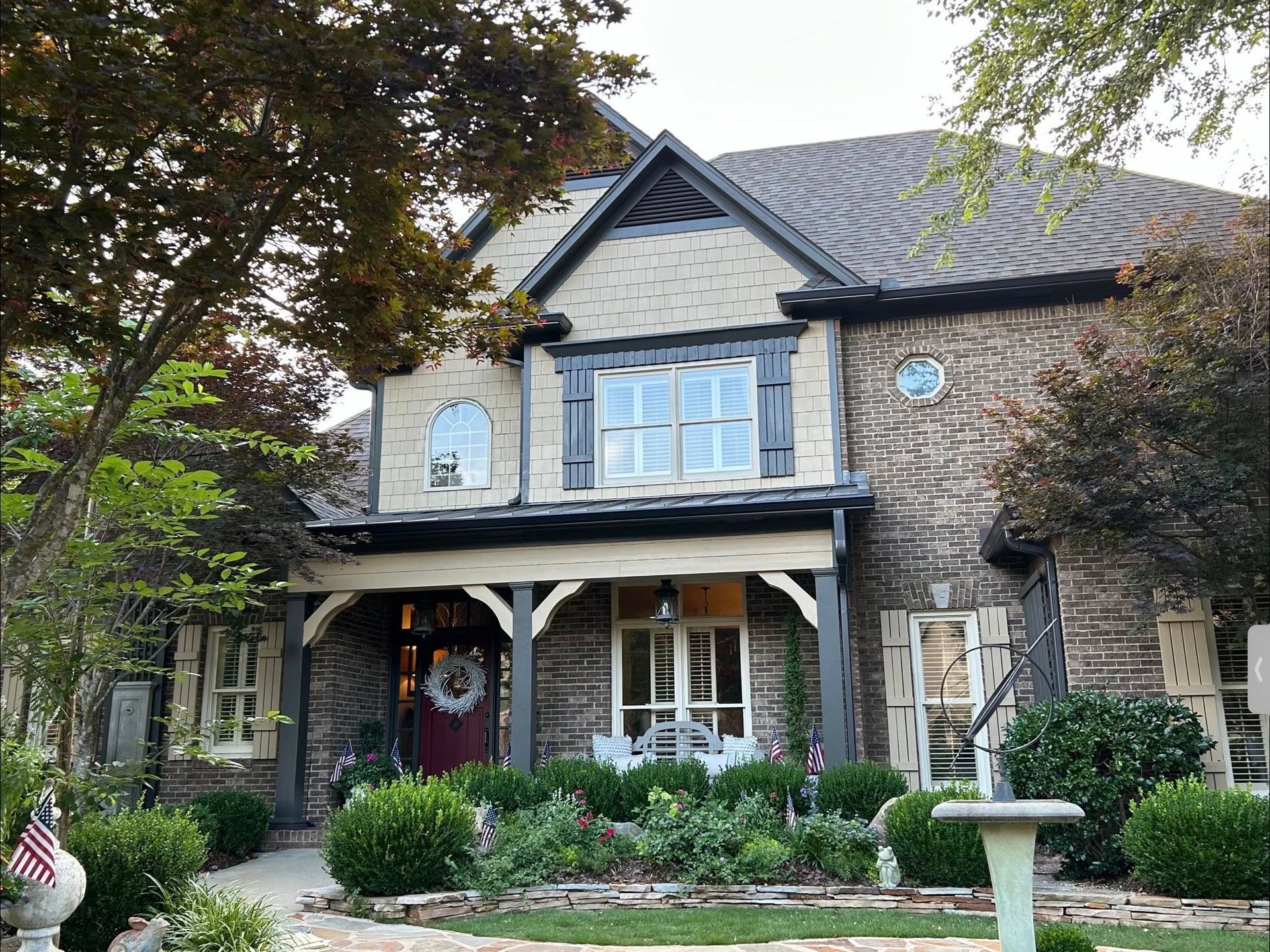 Two-story brick house with a front porch, flower beds, and a fountain in front.