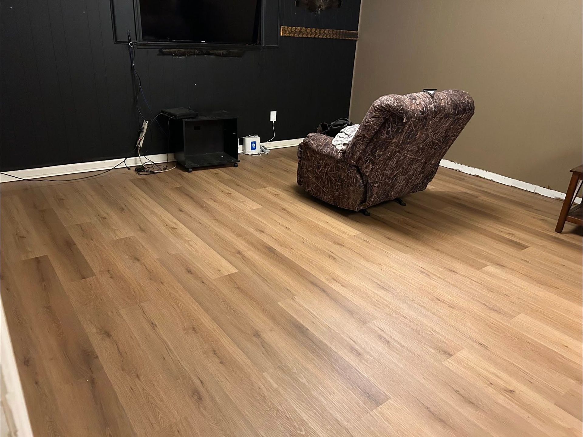 Wood-look flooring in a room with a recliner, black wall with TV, and a side table.