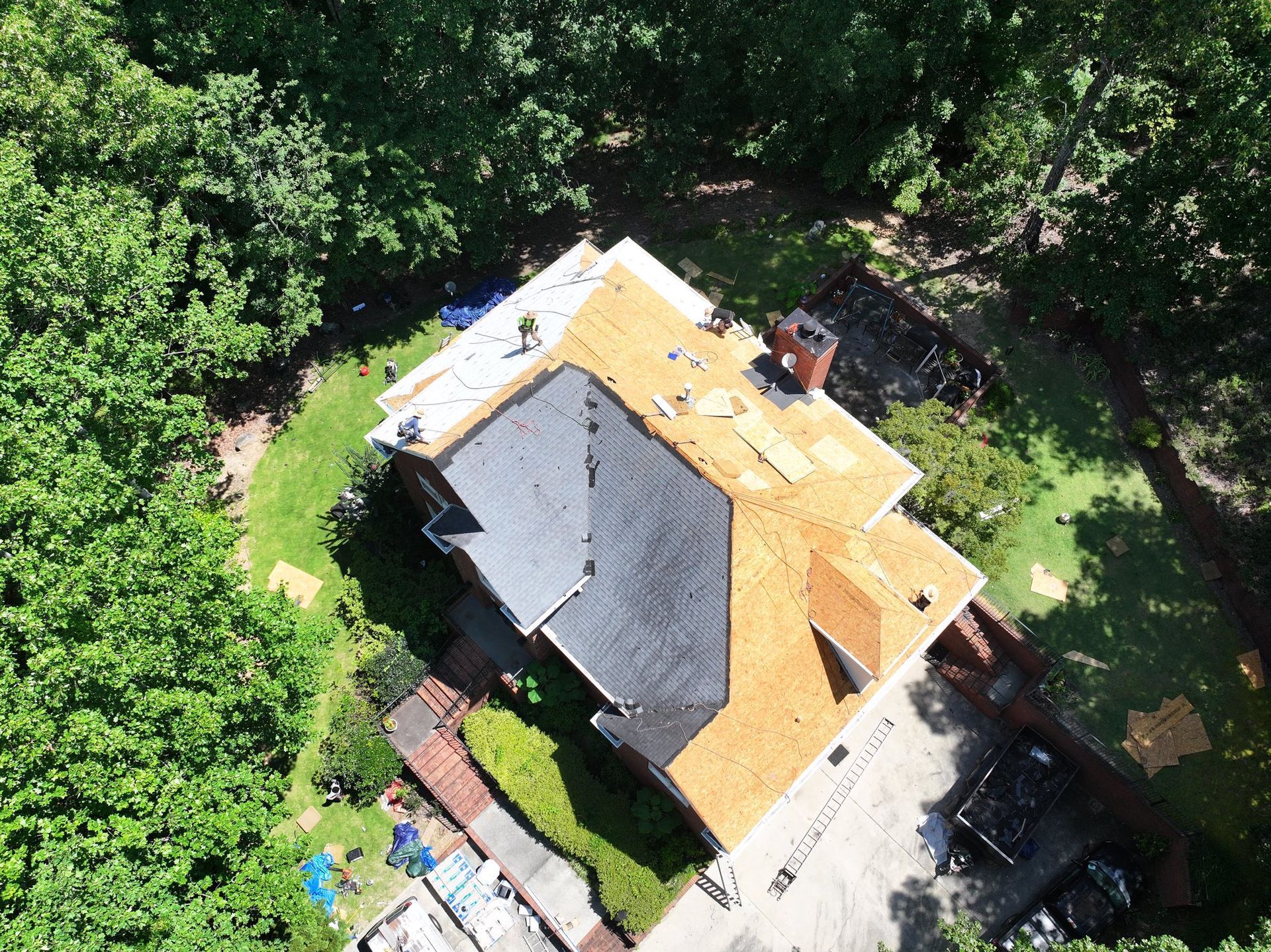 Aerial view of a house roof partially covered with new shingles; workers on the roof.