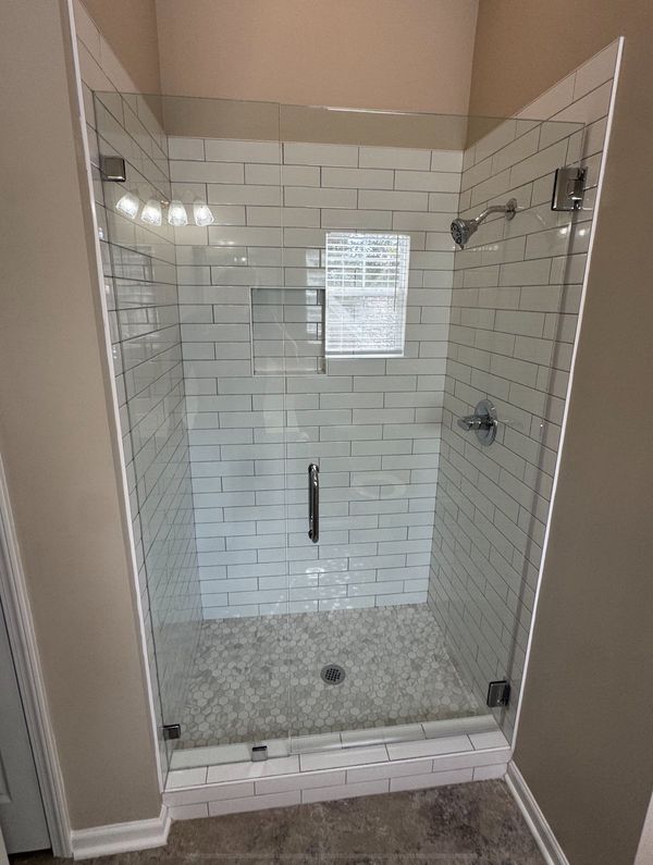 Glass-enclosed shower with white subway tile walls and pebble floor.