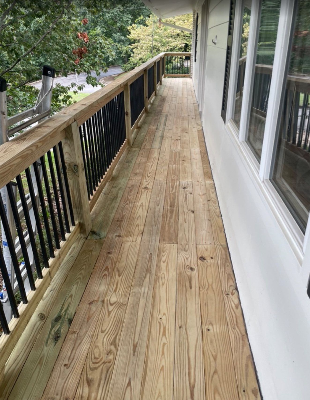 Wooden deck with black railing and white building wall.