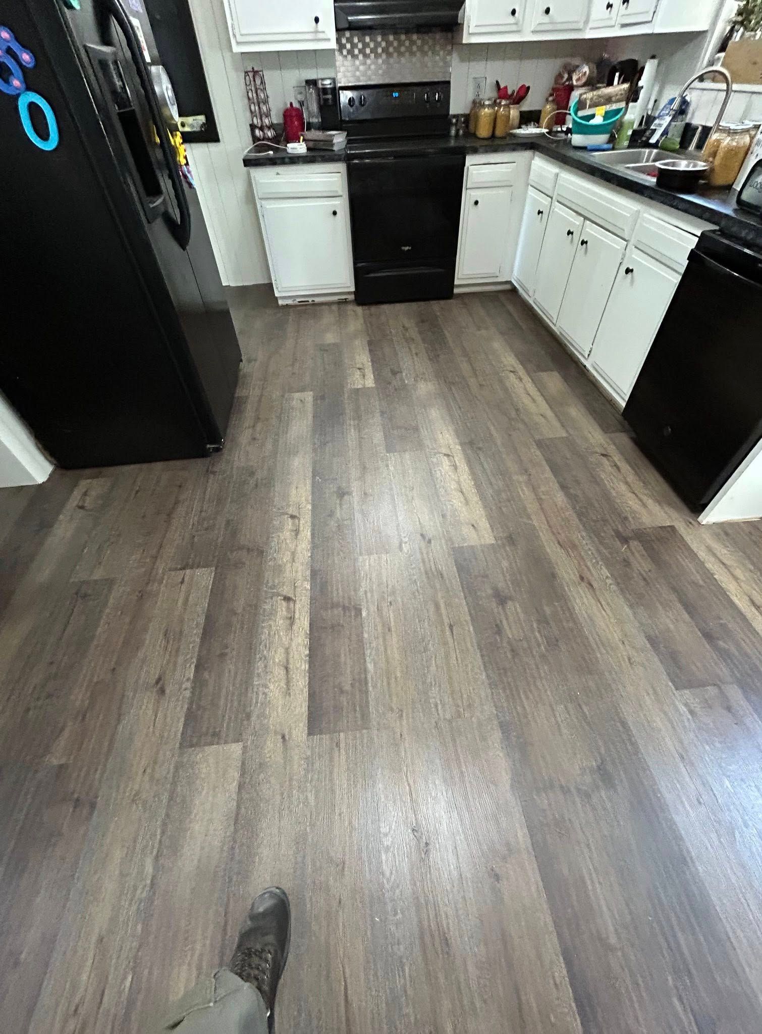 Kitchen with dark wood-look flooring. Black appliances, white cabinets, and a partially visible foot.