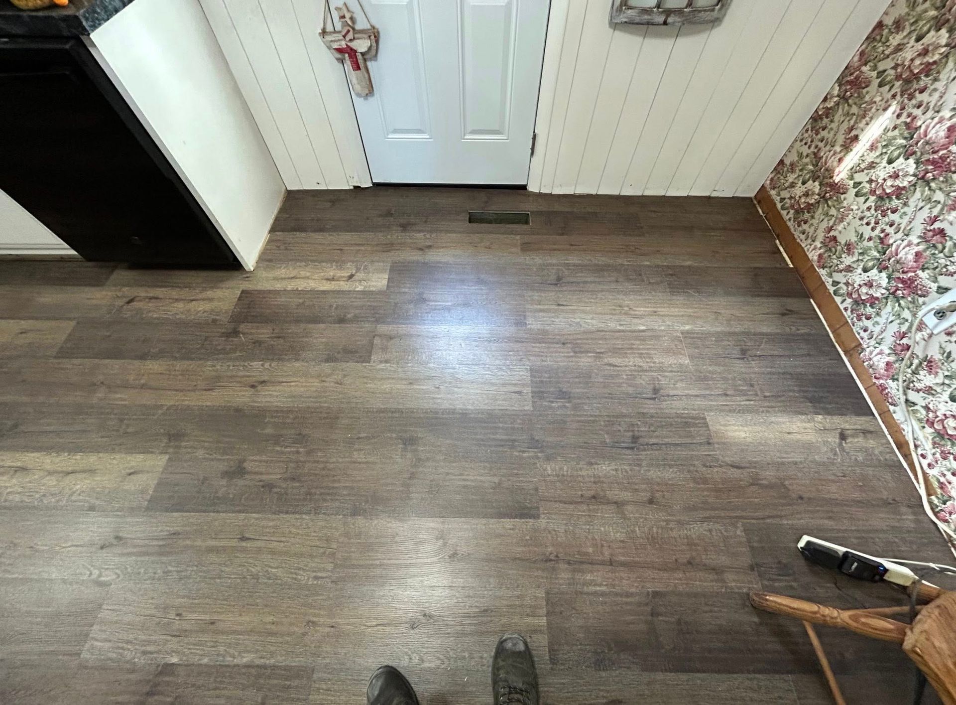 Wooden floor in a hallway with a white door and floral wallpaper.