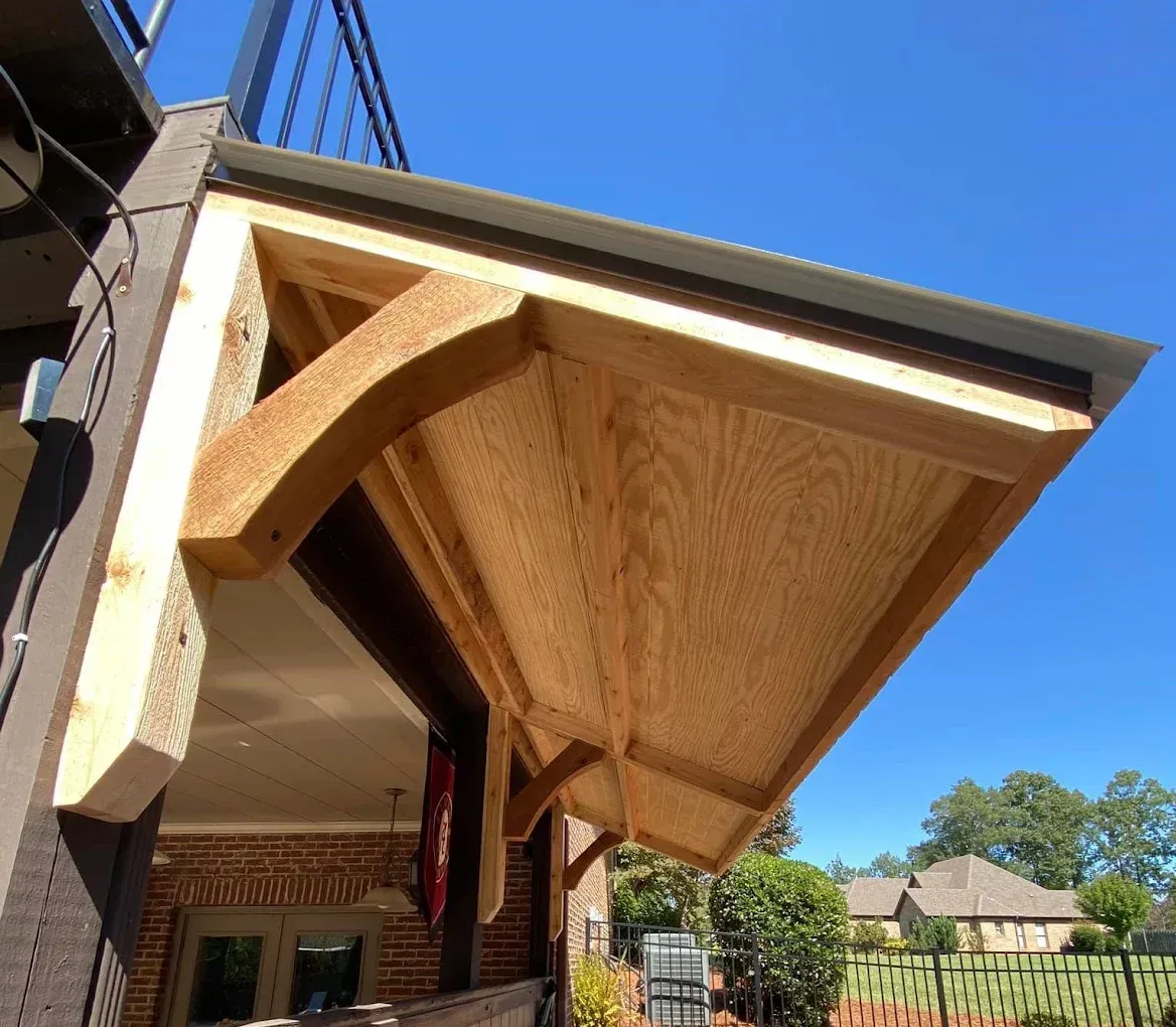 Wooden awning extending from a porch roof, supported by curved brackets. Blue sky above.