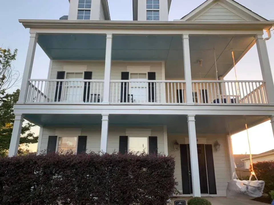 Two-story white house with a porch and swing. Blue ceiling on porch. Dark shrubs in front.
