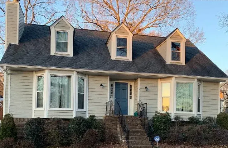 A light-colored house with a dark roof and three dormers. A blue door and front steps are visible.