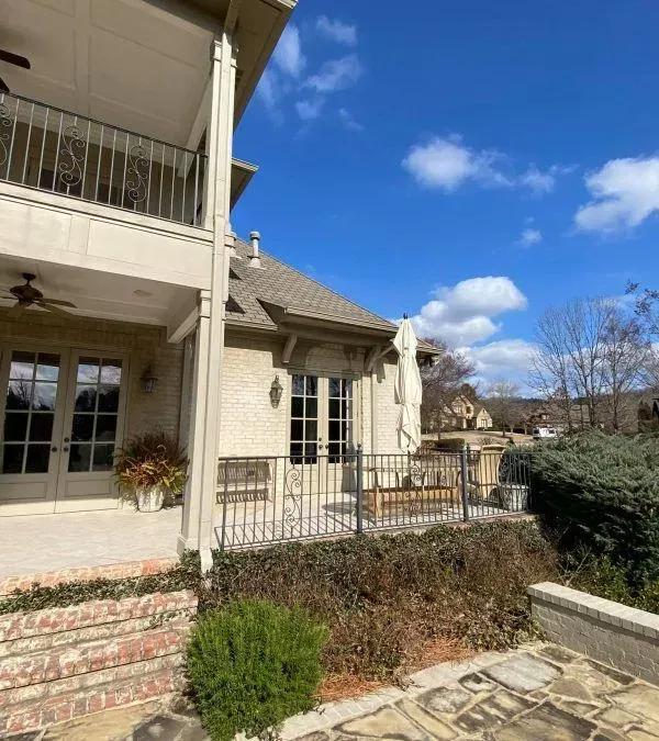 Exterior of a multi-story brick house with a balcony, patio, and blue sky.