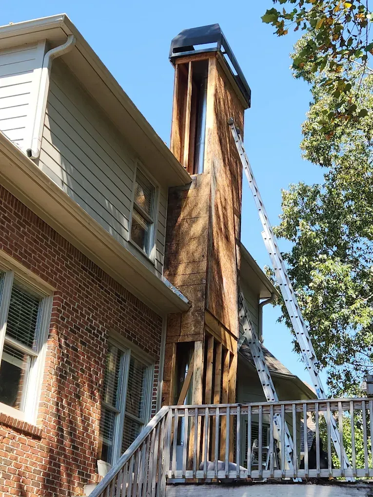 Chimney under repair on a brick and siding house with a ladder propped up.