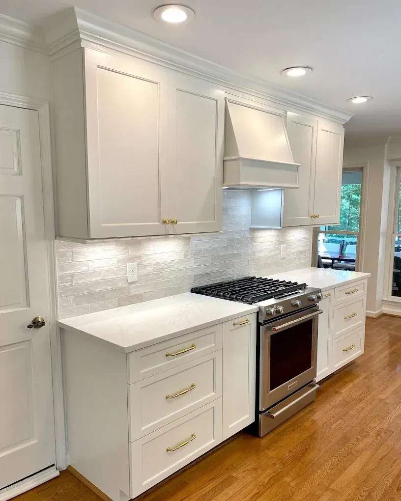 White kitchen cabinets and counters, stainless steel stove, and gold hardware.