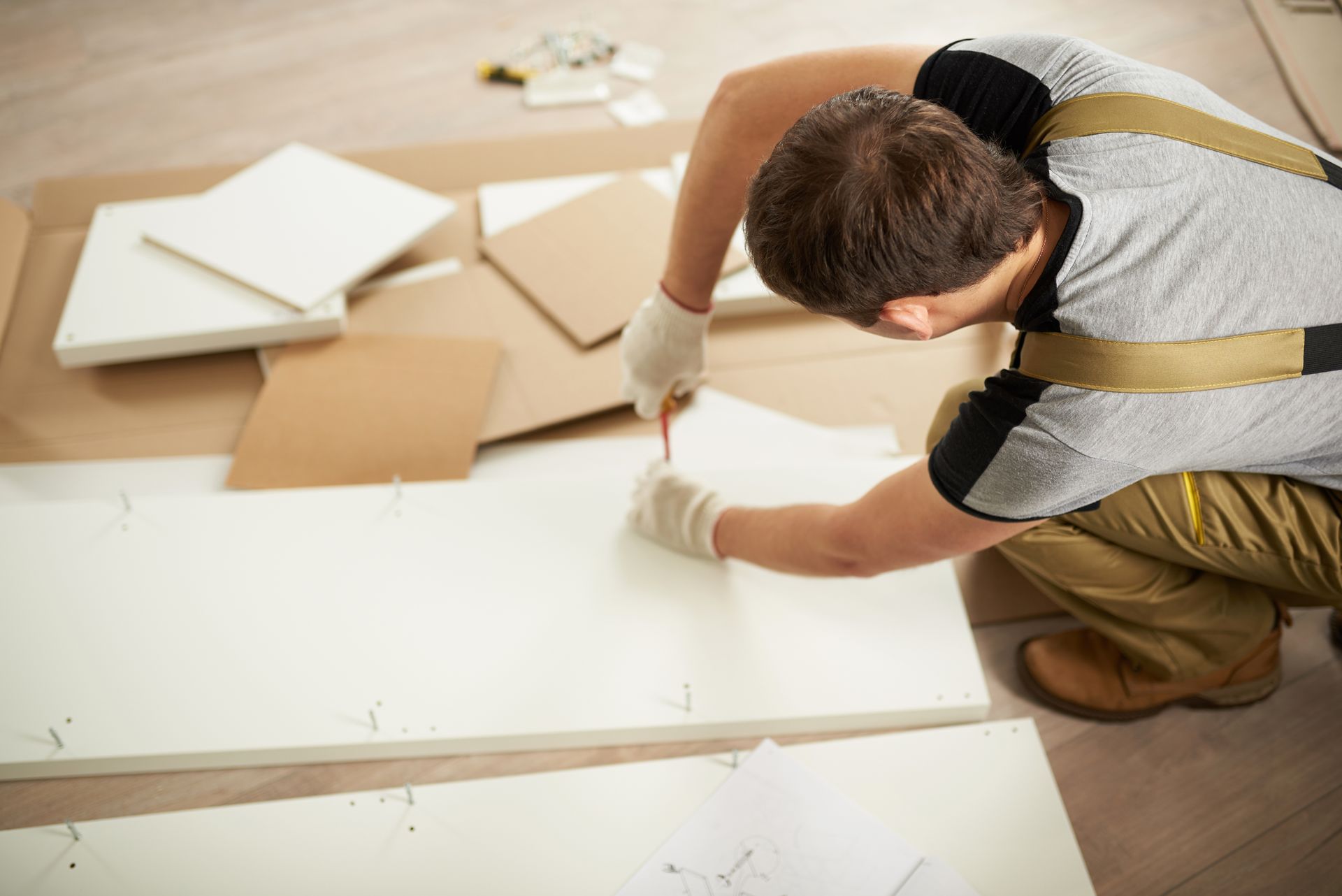 A man is kneeling on the floor while working on a piece of wood.