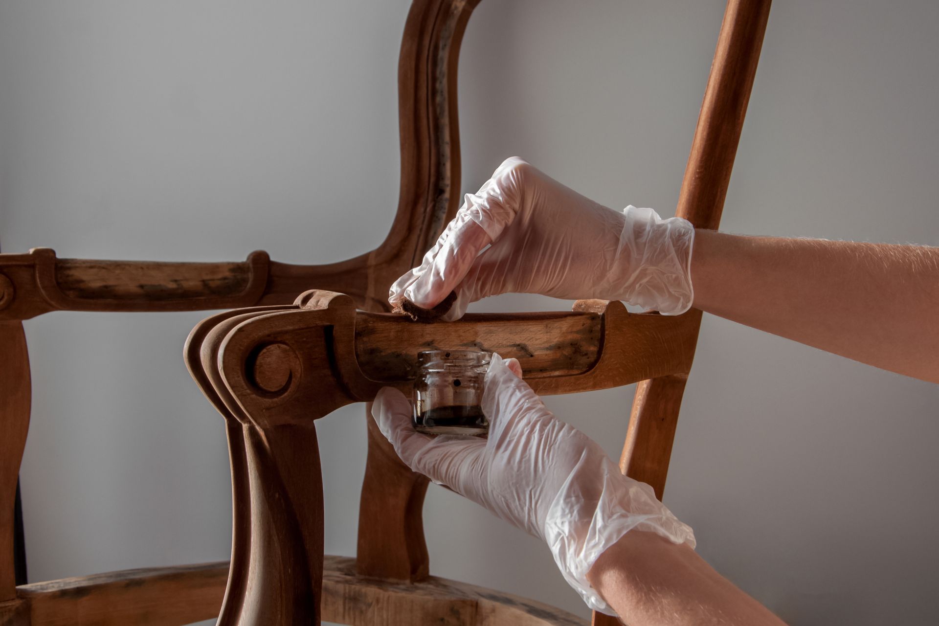 A person wearing white gloves is painting a wooden chair.