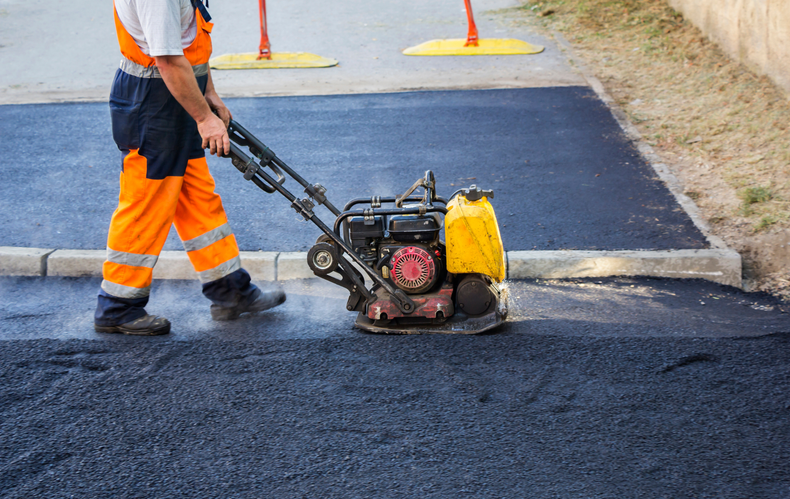 A man is using a machine to compact asphalt on a road.