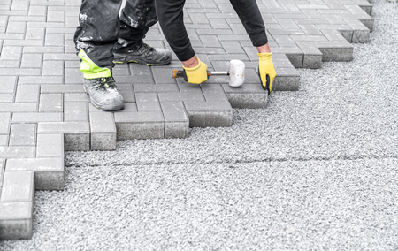 A person is laying bricks on a sidewalk with a hammer.