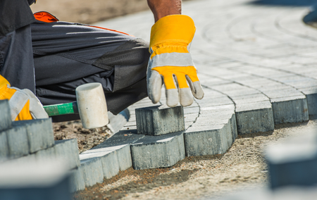 A man wearing yellow gloves is laying bricks on a sidewalk.