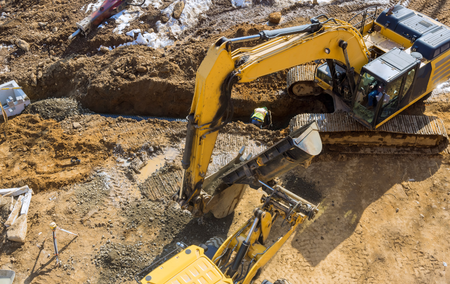 A yellow excavator is digging a hole in the dirt on a construction site.
