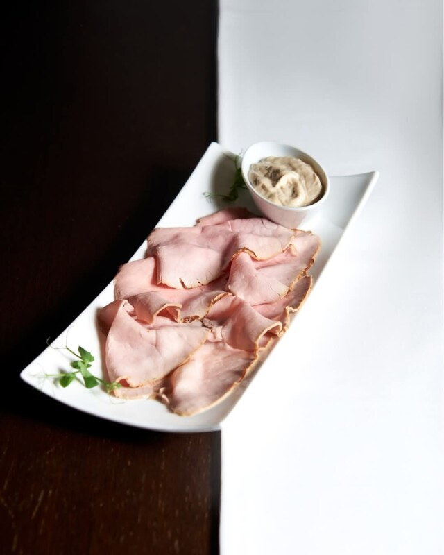 Prosciutto affettato su un piatto bianco accanto a una ciotola di senape