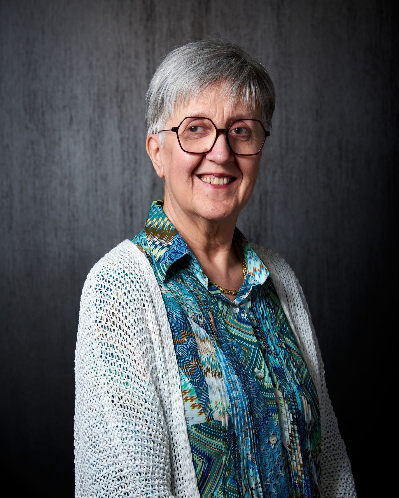 Una donna che indossa occhiali e una maglietta blu sorride alla telecamera.