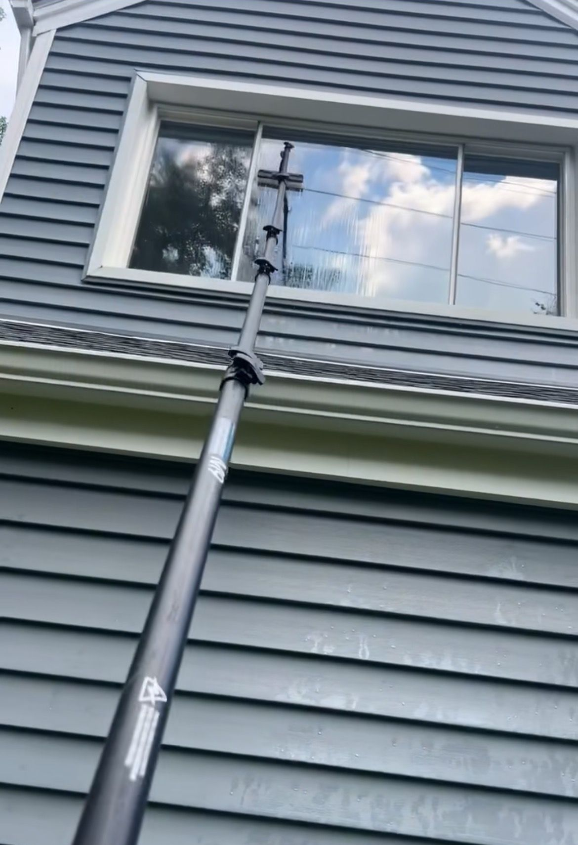 Window cleaner using a pole to wash the second-story window of a house.