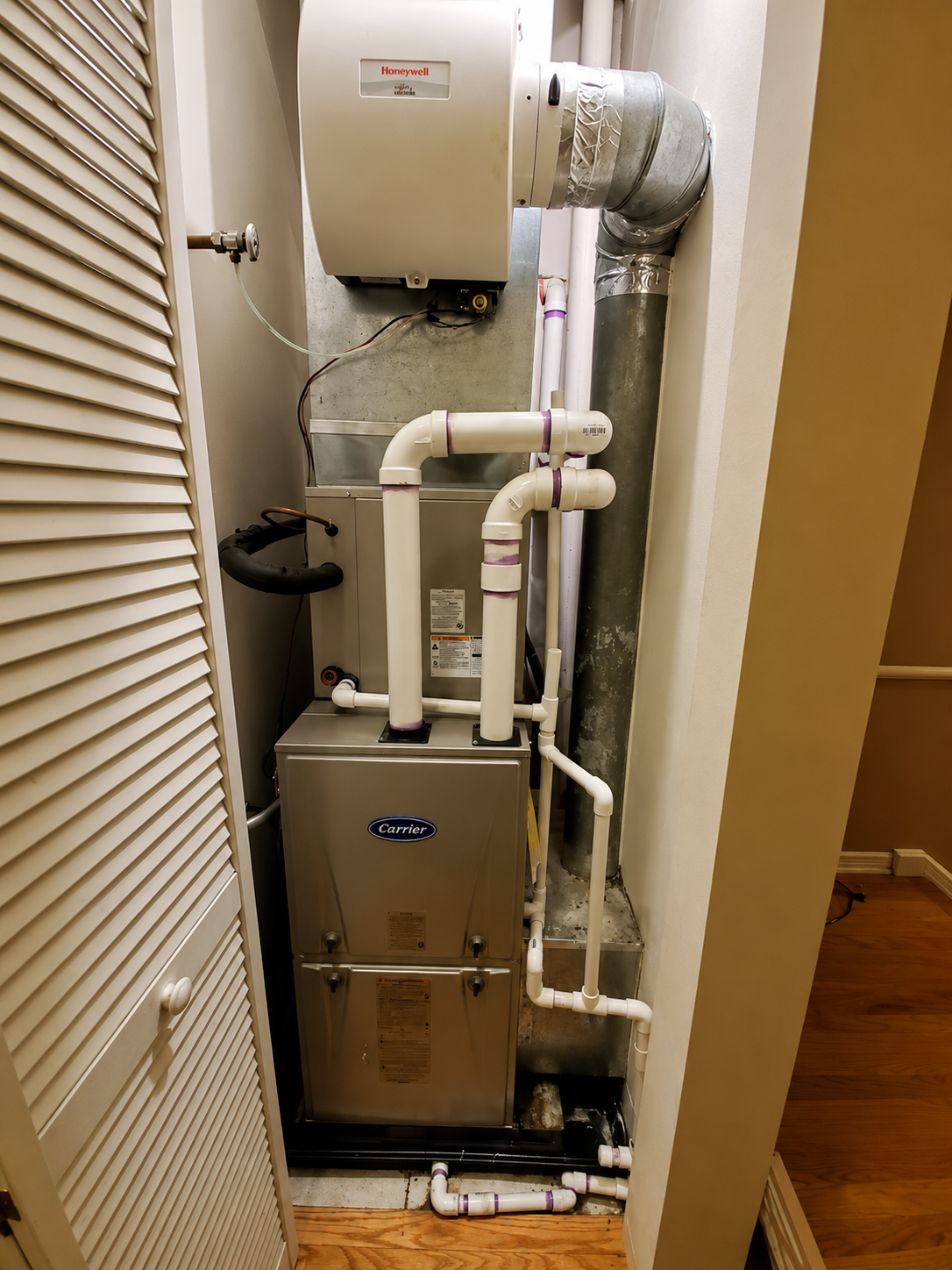 Indoor HVAC closet with a furnace, white ducts, and pipes in a narrow utility space