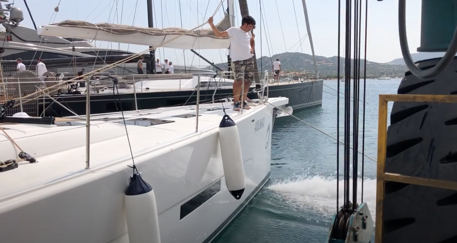 A man is standing on the deck of a sailboat in the water. A Jet Thruster water jet is visible at the bow