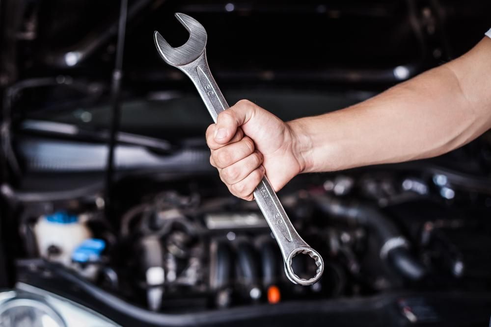 A Person is Holding a Wrench in Front of a Car Engine — C & K Maintenance In Kawana, QLD