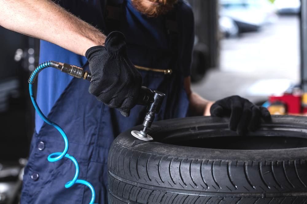 A Man is Working on a Tyre in a Garage — C & K Maintenance In Kawana, QLD